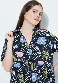 Kortärmad klänning i marinblått tyg med ett blommönster i rosa, blått och grönt. Har krage, knappslå och draperad midja.