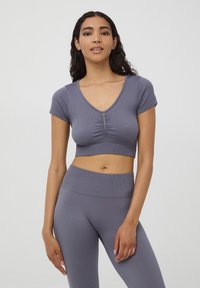 Szara, prążkowana crop top z krótkimi rękawami, głębokim dekoltem w serek i marszczeniem na środku. W połączeniu z pasującymi legginsami w wysokim stanie.