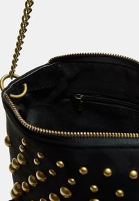Borsa nera con borchie dorate e zip. Interno dotato di una piccola tasca con zip. Cinghia a catena attaccata ai lati. Tessuto testurizzato.