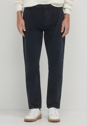 Pantalons en velours côtelé bleu marine à coupe droite, dotés de plis sur le devant et d'une fermeture à bouton. Associés à des baskets blanches pour un look décontracté.