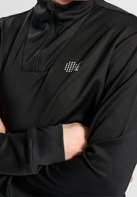 Czarny półzapinany dres z gładkiego, odprowadzającego wilgoć materiału. Posiada wysoki kołnierz i małe logo w odblaskowych kropkach na piersi.