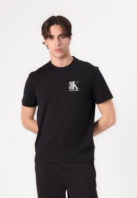 Black cotton t-shirt featuring a small white "ck" logo and "Calvin Klein" text on the chest; classic crew neck and short sleeves.