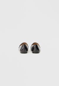 Scarpe slip-on in pelle nera con punta arrotondata, superficie liscia, design minimale e tacco basso. L'interno è foderato in beige.