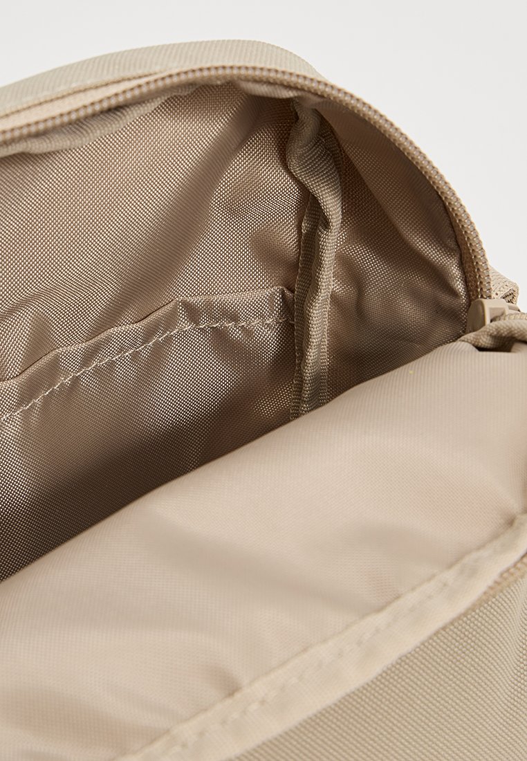 Intérieur d'un sac en tissu beige avec une texture lisse, fermeture éclair, et une poche en mesh sur un côté. Coutures piquées et doublure en tissu étroite.