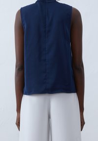 Granatowa bluzka bez rękawów z wysokim dekoltem, wykonaną z miękkiego materiału i o prostym kroju. Posiada centralny szew na plecach i minimalne wykończenia.