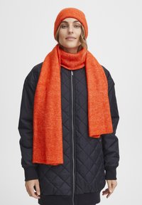 Oranž villane beanie ja sall, mõlemad tekstuuriga ja sooja, koos musta tikandiga jopega, millel on lukuga ees ja soonikkoes mansetid.