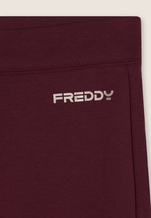 Leggings color bordeaux realizzati in un tessuto morbido ed elastico con una texture liscia. Presentano un logo argento "FREDDY" sulla vita.