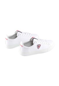 Sneakers bianche basse con una finitura in pelle liscia, dettagli rossi e blu sulla linguetta, e un patch con logo sul lato e sul tallone.