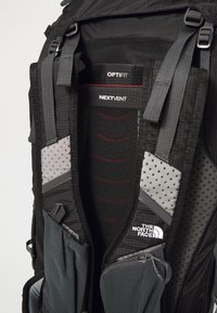 Intérieur d'un sac à dos noir avec des poches en mesh, un rembourrage rouge et noir et des accents gris. Comprend des sangles réglables avec une marque visible.