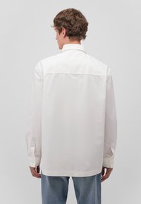 White cotton shirt with a classic collar, long sleeves, and buttoned cuffs. Smooth texture, straight cut, and simple design.