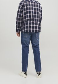 Ensemble deux pièces avec une chemise en flanelle à carreaux marine et un jean bleu, associé à des baskets blanches. Coutures visibles sur le jean.