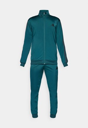 Turf groene trainingspak met een ritsjack met hoge kraag en bijpassende broek. Gemaakt van gladde, ademende stof met zwarte accenten.