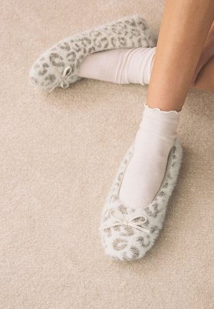 Noge u bijelim čarapama i pahuljastim papučama s leopardskim uzorkom i mašnama, odmara se na bež tepihu.