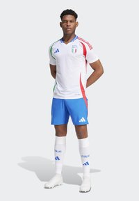 Taliansky národný futbalový dres v bielej farbe s červenými a zelenými detailmi, doplnený modrými šortkami. Obsahuje logo Adidas a nápis "ITALIA" na ponožkách.