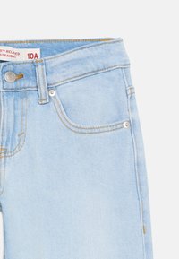 Ανοιχτό μπλε τζιν με πορτοκαλί ραφές, μπροστινή τσέπη, μεταλλικά καρφιά, κλείσιμο με κουμπί και ετικέτα με την επιγραφή 10A relaxed straight.