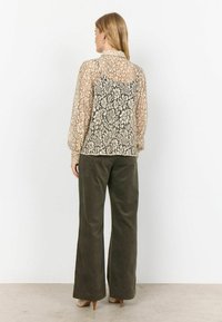 Lace blouse in beige with black floral patterns, long puff sleeves, and a collar, paired with olive green wide-leg pants.