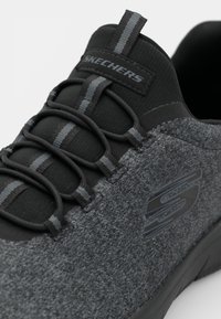 Skechers shoes with a black and gray heathered upper, elastic laces, and a rubber sole. Features a prominent logo on the side.