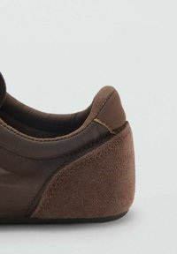 Scarpa marrone con una tomaia in tessuto liscio e un tacco in suede testurizzato. Forma arrotondata con dettagli cuciti e una leggera sfumatura di colore.
