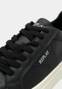 Μαύρο δερμάτινο αθλητικό παπούτσι με στρογγυλή μύτη, μαύκα επίπεδα κορδόνια και λευκό λογότυπο "REPLAY". Διαθέτει αντίθετη υπόλευκη σόλα και λεία υφή.