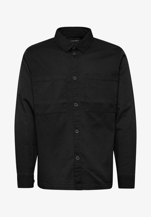 Chemise noire à manches longues en coton, avec un col à bouton, deux poches poitrine et un logo discret sur la poche de gauche.