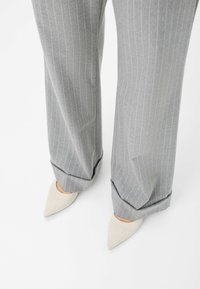 Grijs gestreepte broek met een losse pasvorm, omgeslagen bij de enkels, gecombineerd met lichtbeigepuntige hakken. Gladde stoftextuur.