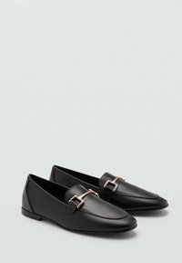 Zwarte leren loafers met een spitse neus, voorzien van een gouden gespaccent op elke schoen, gladde textuur, lage profielzool.