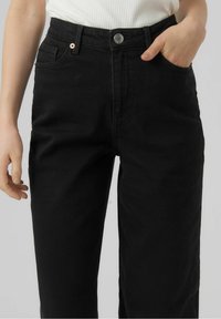 Jeans de mezclilla negra de cintura alta, con dos bolsillos delanteros, un cierre de botón sencillo y un diseño de pierna recta. Textura suave.