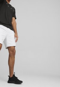 Černé tričko s krátkým rukávem a bílým logem na hrudi, spárované s bílými sportovními šortkami a černými teniskami. Hladká tkanina a pohodlný střih.