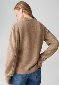 Maglione marrone chiaro lavorato a maglia con vestibilità rilassata, orlo a coste e maniche lunghe. La texture appare morbida e pelosa, progettata per un uso casual.
