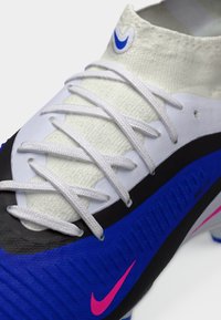 Ποδοσφαιρικό παπούτσι Nike με λευκό επάνω μέρος, μπλε και μαύρες λεπτομέρειες, υφή επιφάνειας και ροζ λογότυπα. Διαθέτει σύστημα κορδονιών κανονικού τύπου.