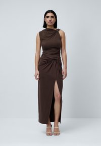 Brun, ermeloft maxi-kjole med drapert design, sidesprekk og knyttedetalj i livet. Brukt med lyse sandaler med stropper.