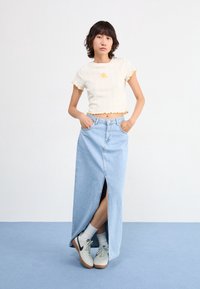 Lightweight cropped ribbed top with ruffled edges and yellow embroidery, paired with a long light blue denim skirt featuring a front slit, and white sneakers.