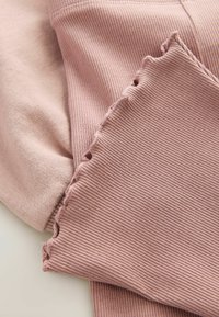 Gros plan sur un tissu rose poussiéreux côtelé avec des bords froncés posé sur un tissu rose clair et lisse.