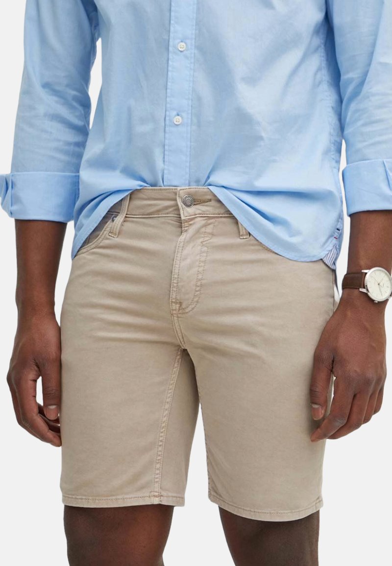 Shorts de algodón beige con un corte ajustado, que cuentan con cierre de botón y cinco bolsillos. Combinados con una camisa de manga larga azul clara.