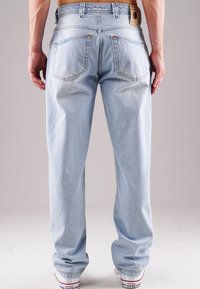 Hellblaue Denim-Jeans mit lockerer Passform, ausgestattet mit zwei Gesäßtaschen, Kupfernieten und einem braunen Lederpatch am Bund.