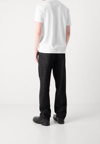 Weiße Kurzarm-T-Shirt kombiniert mit dunklen Jeans. Das Outfit hat eine lockere Passform und ein schlichtes, minimalistisches Design. Schwarze Schuhe.