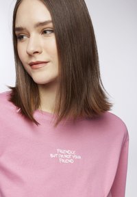 Felpa rosa in cotone con maniche lunghe, decorata con testo bianco che recita "Amichevole, ma non sono tua amica" sulla parte anteriore.