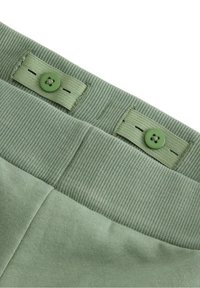 Zielony pas w spodniach z bawełny z dwoma zielonymi guzikami. Żebrowana faktura i gładki materiał. Małe detale przeszycia przy miejscu guzików.