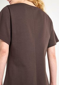 Brun bomulds t-shirt med korte ærmer og rund halsudskæring, med syninger ned ad ryggen, glat tekstur.