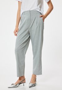 Pantalons ajustés gris clair avec une texture lisse, ornés de plis sur le devant et de poches latérales. Associés à des talons slingback argentés métalliques.