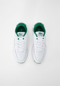 Sneaker bianchi con una texture in pelle liscia, dettagli verdi sulla linguetta e sul rivestimento interno, dotate di un sistema di allacciatura centrale e logo del brand.