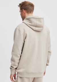 Sweatshirt à capuche beige, fabriqué à partir d'un tissu doux. Présente une coupe décontractée, des manches longues et une poche kangourou. Texture lisse, coutures minimales.