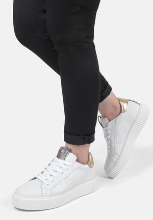 White sneaker with a textured design, featuring a metallic gold accent at the heel and a contrasting silver detail on the tongue.