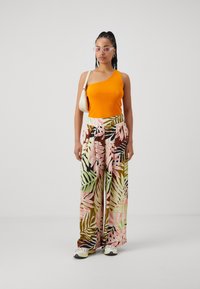 Top naranja de un solo hombro, pantalones de pierna ancha con patrones de hojas rosas y verdes. Footwear cuenta con una suela de color claro con un diseño texturizado.