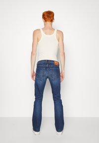 Jeans de mezclilla de tiro alto en azul oscuro con un diseño clásico de bolsillo trasero y una etiqueta de cuero marrón en la cinturilla, combinados con una camiseta sin mangas blanca.