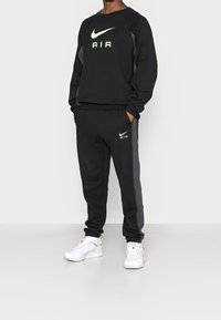 Sudadera negra de Nike con el logo "AIR" en verde lima, combinada con pantalones deportivos a juego que tienen rayas laterales. Llevado con zapatillas blancas.