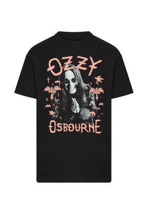 Fekete pamut póló, amelyen grafikai nyomat látható egy hosszú hajú, napszemüveget viselő figuráról, pálmafák és denevérek társaságában, rózsaszín szöveggel.