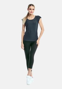Black short-sleeve athletic top paired with black leggings and white sneakers. Smooth fabric with a fitted design. Simple styling.