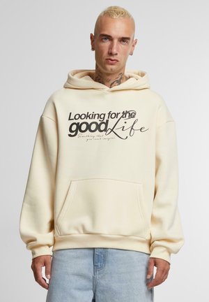 Kremfarget hettegenser med frontlomme, elastiske mansjetter og trykket tekst "Looking for the good Life" i mørke og lyse fonter.