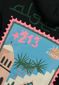 Zwarte stof met een kleurrijk grafisch ontwerp dat lijkt op een postzegel. Bevat palmbomen, architectuur en de tekst "+213" in roze.